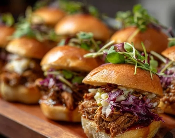 Apple cider pulled pork sliders with pomegranate bourbon BBQ sauce on a platter.